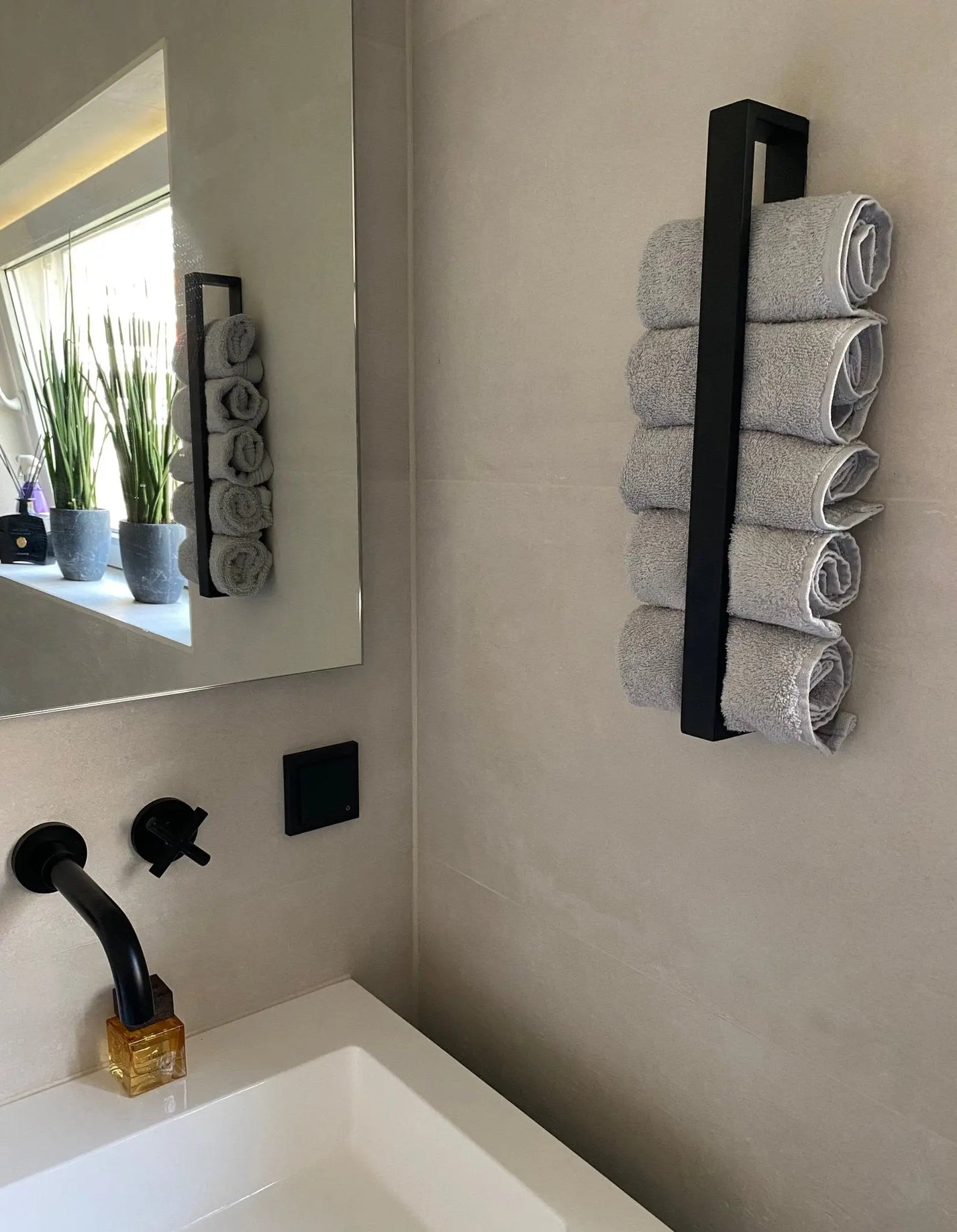 Modern zwart handdoekrek met opgerolde handdoeken in een badkamer